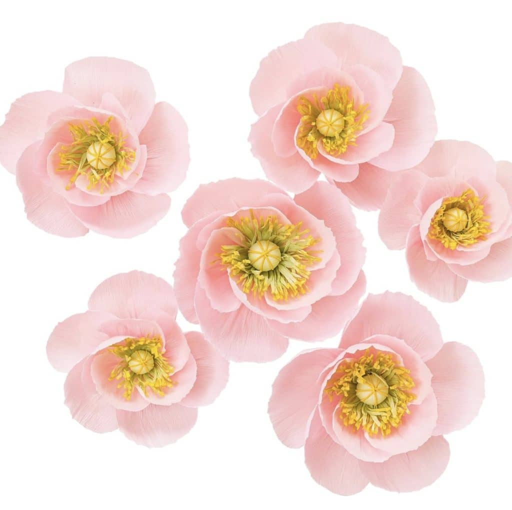 Six pink paper peonies with intricate yellow centers are arranged against a white background. The delicate petals and lifelike details evoke the charm of a DIY flower project, adding a sense of lightness and elegance to any space.